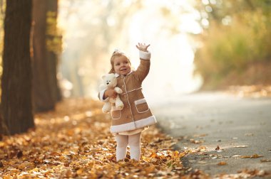 Beyaz oyuncak ayıcık ellerinde. Tatlı küçük kız sonbahar ormanında dökülen yapraklarla..