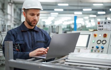 Dizüstü bilgisayarı kullanarak. Fabrika işçisi kasketli bir şekilde içeride..