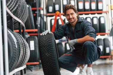 Oturup lastiği gösteriyor. Lastik tamir servisinde adam var..