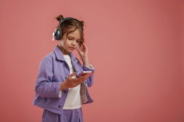Akıllı telefon ve kulaklık. Şirin küçük kız pembe arka plana karşı..