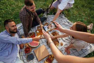 Akıllı telefon kullanarak fotoğraf çekmek. Bir grup arkadaş, ekolojik kutularda yiyeceklerle sahada piknik yapıyorlar..