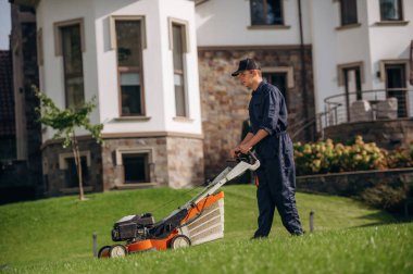Yandan manzara, çim biçme makinesiyle çim biçme. Bahçede profesyonel bahçıvan var..