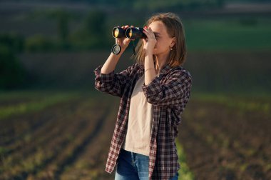 Dürbünden bakıyorum. Gündüz vakti güzel tarla tarlasında genç bir kadın var..