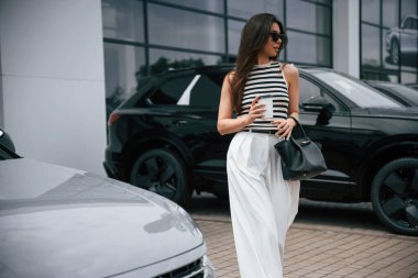 Beyaz bir kadeh ile. Çekici genç bayan dışarıda, yepyeni arabasının yanında..