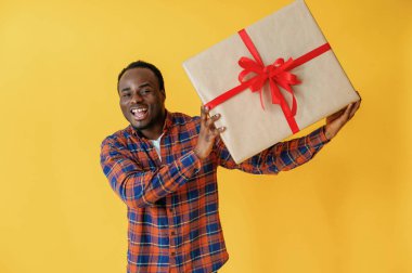 Büyük hediye kutusuyla. Siyah adam sarı arka planda stüdyoda..