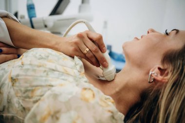 Yan görüş. Kadın uzanıyor ve tiroid bezinin ultrasonik testinden geçiyor..