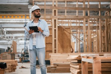 Bitmemiş proje, elinde dijital tablet var. Ahşap depoda sanayi işçisi..