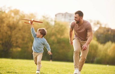Yaz mutluluğu. Oyuncak uçakla koşuyor. Baba ve oğul sahada eğleniyorlar..