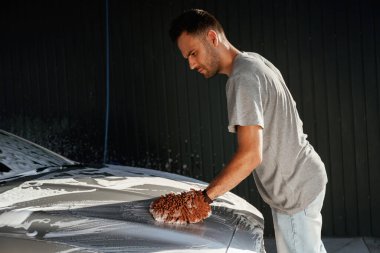 Otomobili yıkamaya odaklanmış. Adam dışarıda arabasıyla bekliyor..