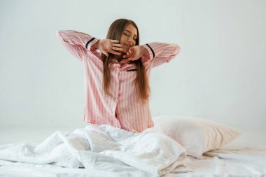 Ön manzara, pembe pijamalı, uyanıyor. Genç ve güzel bir bayan stüdyoda arka plana karşı..