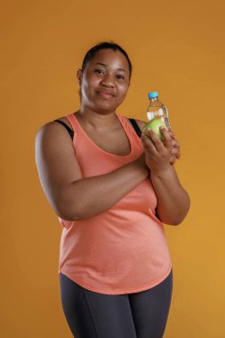Ellerinde yeşil elma ve bir şişe su. Afrikalı Amerikalı kadın sarı arka planda stüdyoda..
