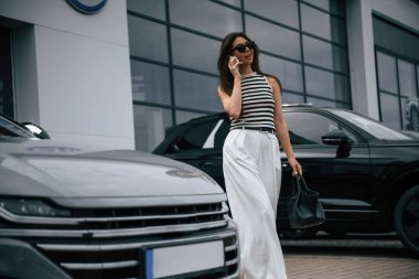 Telefonla konuşuyorum. Çekici genç bayan dışarıda, yepyeni arabasının yanında..