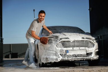 Beyaz temizlik kimyasalı, otomobili yıkamak. Adam dışarıda arabasıyla bekliyor..