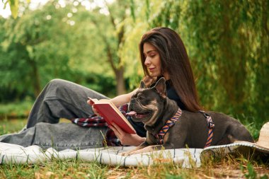 Hikaye okuma, kırmızı kitap. Genç güzel bayan köpeğiyle birlikte parkta..