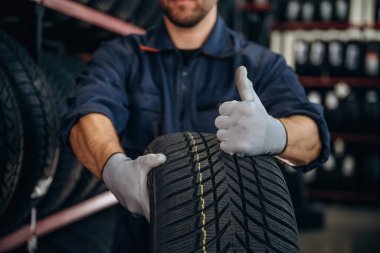 Yakın görüntüye odaklanmış, başparmak yukarıda, lastik tutuyor. Erkek işçi tekerlekleri olan bakım istasyonudur..