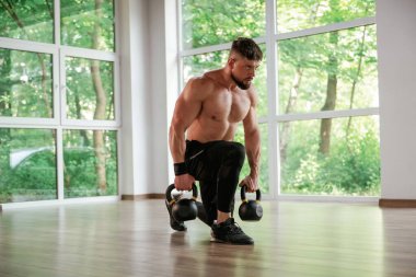 Kalkıyor, dambılları tutuyor. Güçlü kaslı adam spor salonunda çalışıyor..