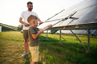 Yüzeyi temizleme zamanı. Baba ve küçük oğlu güneş panellerinin yakınındalar..