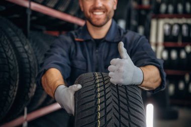 Yakın görüntüye odaklanmış, başparmak yukarıda, lastik tutuyor. Erkek işçi tekerlekleri olan bakım istasyonudur..