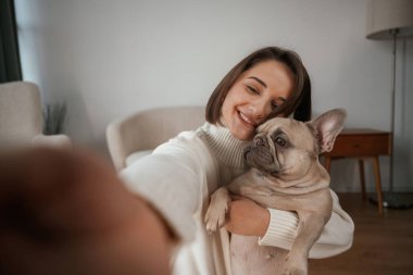 Selfie çekmek, gülümsemek. Genç kadın köpeğiyle evde..