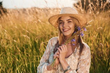 Hasır şapkalı, elinde bitki olan. Güzel genç bayan tarlada, kırsalda.