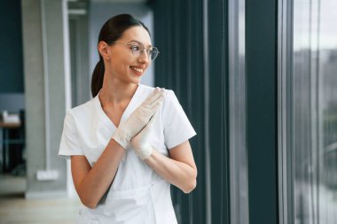 Beyaz önlüklü neşeli bayan doktor içeride ayakta ve gülümsüyor..