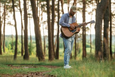 Yakışıklı adam akustik gitarla ormanda..