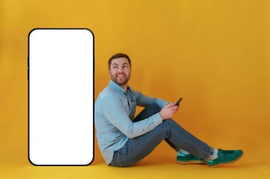 Kopya alanı için büyük akıllı telefonlu. Mavi gömlekli çekici adam sarı arka plana karşıdır..