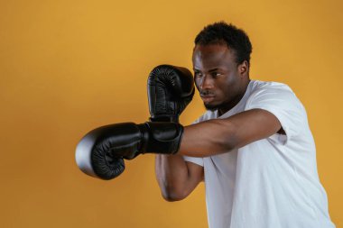 Boks yumruğu alıştırması yapıyorum. Siyah adam sarı arka plana karşı..
