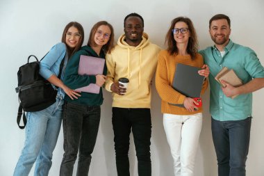 Not defterleri ve kahve fincanı tutuyor. Bir grup genç beyaz arka planda duruyor..