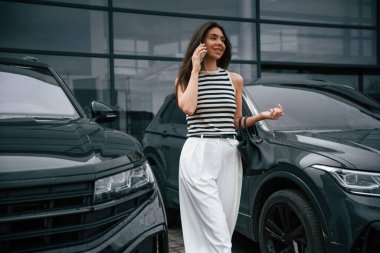 Akıllı telefonlu. Çekici genç bayan dışarıda, yepyeni arabasının yanında..