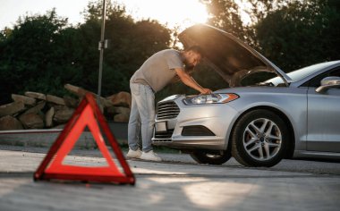 Güneş ışığı altında, kırmızı tabela, kaza, bozuk otomobil, tamir. Adam dışarıda arabasıyla bekliyor..