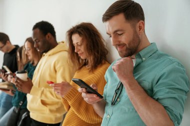 Akıllı telefon kullanmakla meşgul. Bir grup genç beyaz arka planda duruyor..