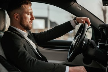 Sürücü, odaklanmış. Siyah takım elbiseli adam arabada oturuyor..