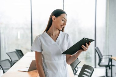 Elinde siyah bir not defteri var. Beyaz önlüklü kadın doktor içeride..