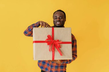 Büyük hediye kutusuyla. Siyah adam sarı arka planda stüdyoda..