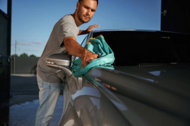 Turkuaz kumaş, aracı cilalama. Adam dışarıda arabasıyla bekliyor..