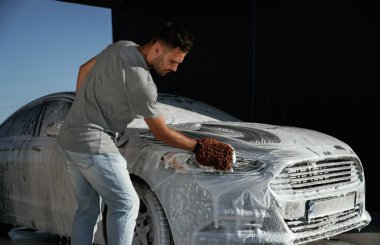 Beyaz sabun ve köpük, otomobili yıkamak. Adam dışarıda arabasıyla bekliyor..