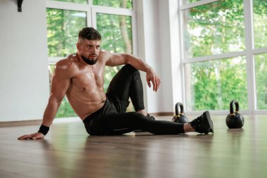 Mola verdim. Dambıllar yere. Güçlü kaslı adam spor salonunda çalışıyor..