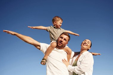 Eller yanlara, uçmak, hayal gücü. Anne ve baba oğluyla birlikte dışarıda, tarlada..