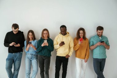 Akıllı telefon kullanmakla meşgul. Bir grup genç beyaz arka planda duruyor..