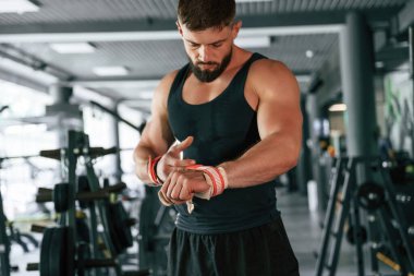Elinde kırmızı koruyucu bandajlar var. Güçlü kaslı adam spor salonunda çalışıyor..