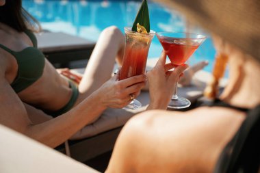 Manzarayı kapat, yan yana otur. İki güzel kadın havuz kenarında dinleniyor..