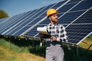 Ellerinde not defteriyle sahada. Gündüz vakti fotovoltaik güneş panelleri olan bir mühendis..