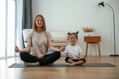 Sakin, nilüfer pozisyonunda. Küçük kızı olan genç bir kadın evde yoga yapıyor..