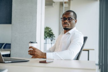 Elinde içkiyle, masanın yanında. İşadamı modern ofiste çalışıyor..