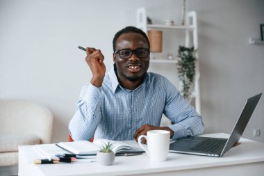 Oturuyor ve gülümsüyor. Elinde kalemle. İşadamı ofiste bilgisayarla çalışıyor..