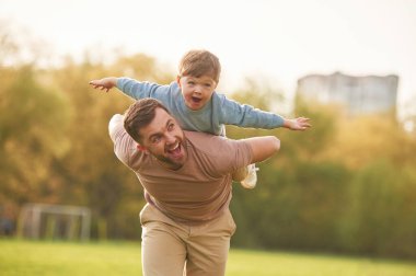 Refah içinde, çocuk ya sırtında ya da omuzlarında. Mutlu baba ve oğul yazın sahada eğleniyorlar..