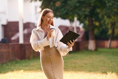 Dijital tablet ve bir bardak içki ellerinde. Güzel kız öğrenci üniversitenin yakınında dışarıda..