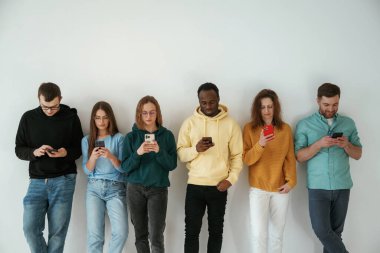 Akıllı telefon kullanmakla meşgul. Bir grup genç beyaz arka planda duruyor..