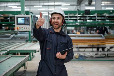 Emirleri elle veriyor. Fabrika işçisi kasketli bir şekilde içeride..